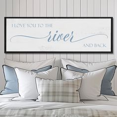 a bed with white sheets and pillows in front of a framed sign that says i love you to the river and back