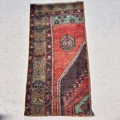 an old rug is laying on the floor next to a white wall with a black and red design