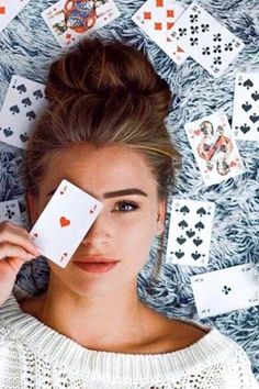 a woman laying on top of a pile of playing cards with her eyes closed and one card in front of her face