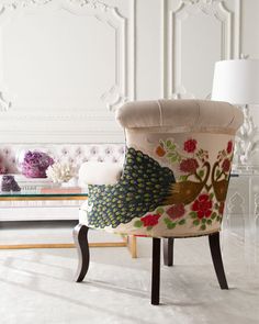 a fancy chair in front of a white wall with flowers on it and a lamp next to it