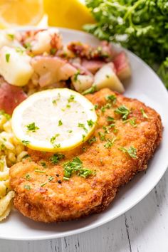 a white plate topped with fish, pasta and veggies next to lemon wedges