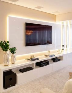 a living room with white walls and large television mounted on the wall above it's entertainment center