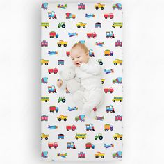 a baby laying on top of a white sheet covered in colorful train cars and trucks