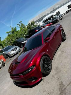 a red sports car parked in a parking lot next to other cars and trucks on a sunny day