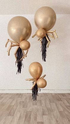 three gold balloons with black ribbons hanging from them