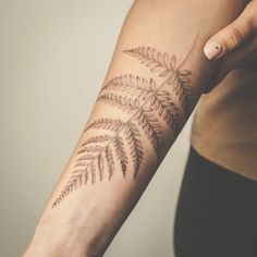 a woman's arm with a fern tattoo on it