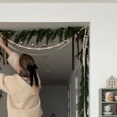 a woman reaching up into the ceiling with christmas garland hanging on it's wall