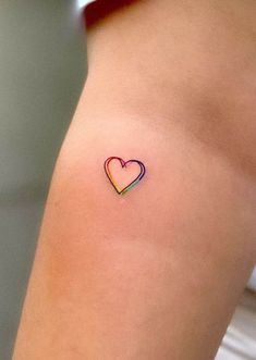 a small heart tattoo on the back of a woman's thigh, with rainbow colors