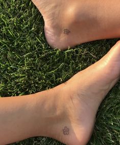 two people with small tattoos on their legs laying in the grass together, one has a paw tattoo on it's left foot