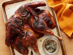 a roasting pan filled with chicken on top of a wooden table next to an orange napkin