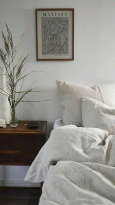 a bed with white sheets and pillows next to a wooden night stand on a hard wood floor