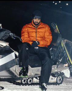 a man in an orange jacket sitting on a snowmobile