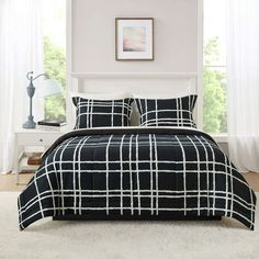 a black and white bed with plaid comforter set on top of it in front of a window