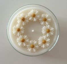 a glass bowl filled with white daisies on top of a table next to a wall