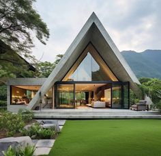 a triangular shaped house in the middle of a lush green field with mountains in the background