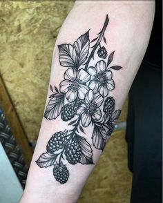 a black and white flower tattoo on the left arm with berries, leaves and flowers