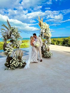 a bride and groom kissing in front of an outdoor ceremony arch with flowers on it