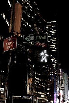 street signs in the city at night with skyscrapers and lights shining on the buildings