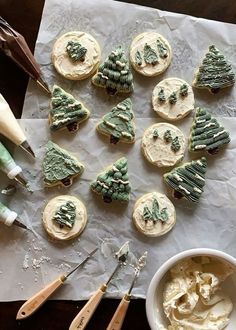 decorated cookies with green icing and trees on them next to a bowl of frosting