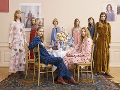 a group of women sitting around a table in front of pictures on the wall behind them