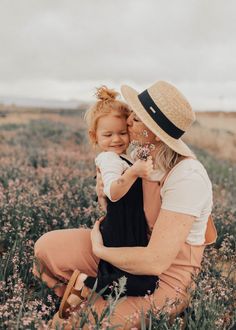 a woman holding a baby in her arms while sitting on the ground with flowers around her