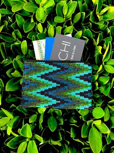 a blue and green wallet sitting on top of a lush green leaf covered ground next to a credit card holder