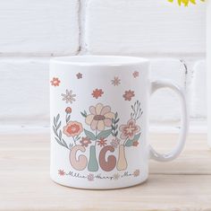 a white coffee mug sitting on top of a table next to a vase with flowers