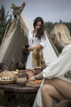 two women sitting at a table with food and a teepee tent in the background