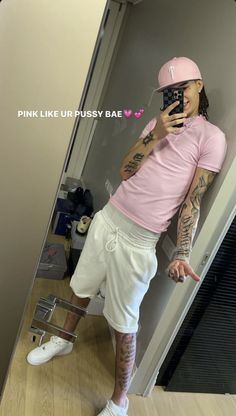 a man with tattoos taking a selfie in a mirror wearing white shorts and a pink t - shirt