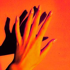 two hands with manicured nails against an orange background