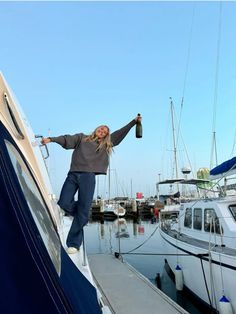 a woman standing on top of a boat next to other boats in the water with her arms outstretched