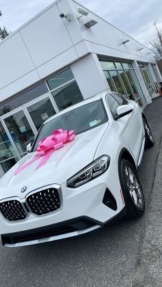 a white car with a pink bow on it's hood parked in front of a building