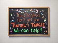 this christmas sign is hanging on the wall in front of a chalkboard that reads, tisel in a tangle we can help