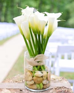 white flowers in a glass vase with rocks and burlocks on a wooden table