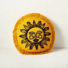 a yellow pillow with a sun design on it's face and fringes around the edges