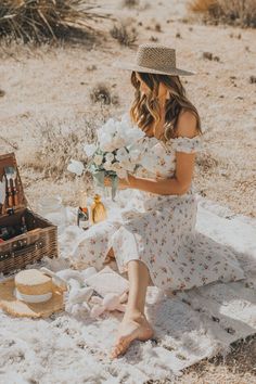 a woman sitting in the sand with a picnic basket