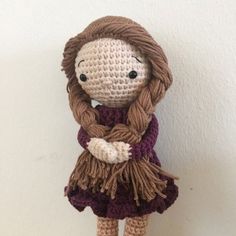 a crocheted doll with long brown hair wearing a purple dress and holding her arms crossed