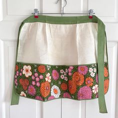 an apron hanging on a door with flowers and green ribbon attached to the front pocket