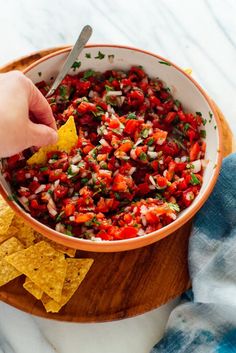 a person dipping salsa into a bowl with tortilla chips