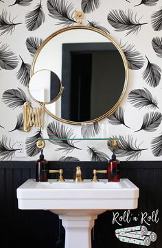 a white sink sitting under a mirror next to a black and white wallpaper covered in leaves