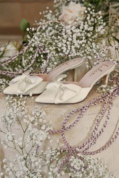 a pair of white high heeled shoes sitting on top of a table next to flowers