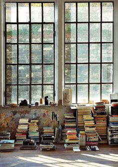 a room filled with lots of books on top of a floor next to two large windows