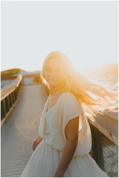 a woman in a white dress standing on a bridge with her hair blowing in the wind