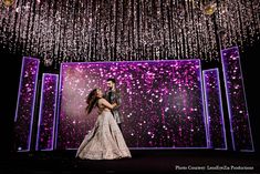 a man and woman standing in front of a stage with lights hanging from the ceiling