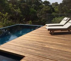 an empty lounge chair sitting on top of a wooden deck next to a swimming pool