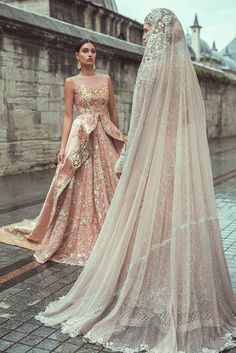 two women dressed in wedding gowns standing next to each other on a brick walkway