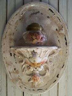 an old white plate with a glass vase on it's side hanging from the wall