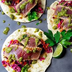 three tortillas topped with meat and veggies next to a lime wedge