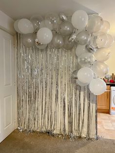 white balloons and streamers are hanging from the ceiling in front of a curtain made of silver foil