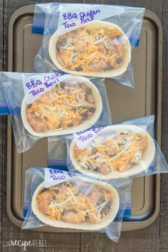 three burritos wrapped in plastic sitting on top of a metal baking pan covered in cheese